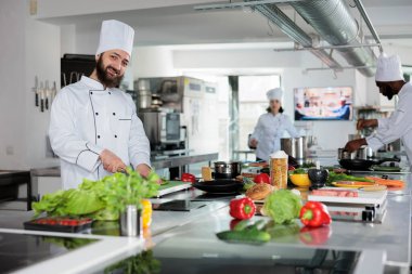 Gurme Kafkasyalı aşçı taze organik sebzeleri keserken akşam yemeği için yemek tarifi hazırlıyor. Gülümseyen baş aşçı garnitür hazırlarken gastronomik yemekler pişiriyor..