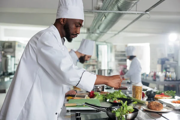 Yemek endüstrisi uzmanı taze yeşil otlar ekliyor. Yemek pişirme üniforması giyen gastronomi uzmanı restoranda akşam yemeği için lezzetli bir gurme yemeği hazırlıyor..