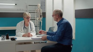 Emekli hasta, reçeteli tedavi ve sağlık desteği almak için randevu kağıdı imzalıyor. Doktor, tıbbi kabinede hasta bir adama danışıyor. Belgeleri imzalıyor..