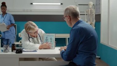 Doktor Osteopath, kontrol ziyaretinde osteopati teşhisine yardımcı olması için dijital tablette insan iskeleti çizimini açıklıyor. Cihazda ortopedik kemik hastalığı ve tıbbi uzmanlık analiz ediliyor..