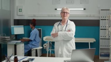 Üst düzey doktorun portresi kabinede kollarını kavuşturup hastaya sağlık ekipmanları kullanarak muayene yapıyor. Sağlık uzmanlığında pratisyen hekimlik yapıyor..