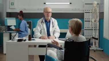 General practitioner consulting woman with chronic disability in medical office, doing checkup examination with medication. Retired patient with impairment and health condition at appointment.