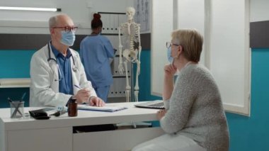 Salgın sırasında kıdemli bir hastanın muayenesine katılan pratisyen hekim. Doktor, yaşlı bir kadına sağlık sistemi ve tedavi uygulamaktan bahsediyor..