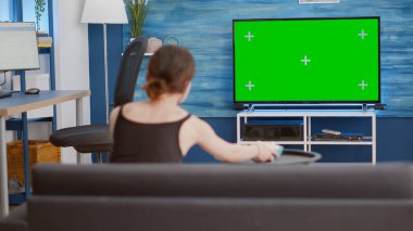 Televizyonda yeşil ekranlı film izleyen ve kanepede otururken patlamış mısır yiyen genç bir kadının statik tripod görüntüsü. Ev oturma odasındaki krom anahtar ekranlı favori televizyon dizisine bakan bir kız..