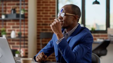 Afrikalı Amerikalı düşünceli bir adam dizüstü bilgisayarla proje planlamak için beyin fırtınası yapıyor. Düşünceli yönetici web sitesindeki sunum raporunu düşünüyor, araştırma e-postası yazıyor.