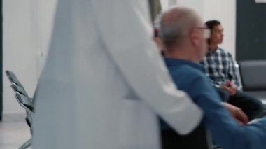 Afro-Amerikalı ve Asyalı hastalar hastane resepsiyonundaki randevular için yardım istiyorlar. Bekleme odasında oturup tıbbi rapor yazan bir sürü insan var. El kamerasıyla..