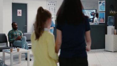 Anne ve küçük kız hastane resepsiyonunda sağlık randevusuna katılmak için check-up raporu yazıyorlar. Destek ve yardım almak için sağlık muayenesi olan hastalar.