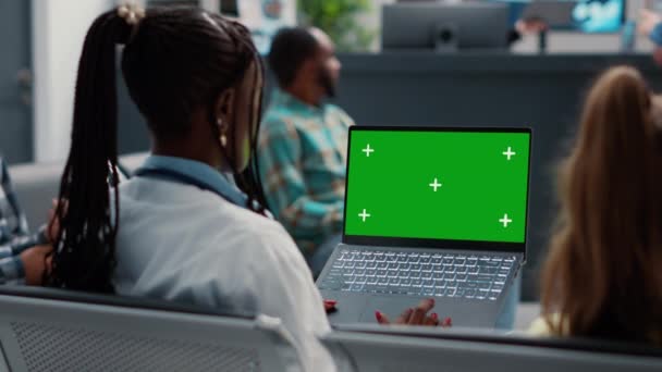 全科医生手持带有绿屏的笔记本电脑在候诊室 坐在医院接待室大堂 博士使用空白模型模板与孤立的复制空间和彩色键 三脚架射击 — 图库视频影像