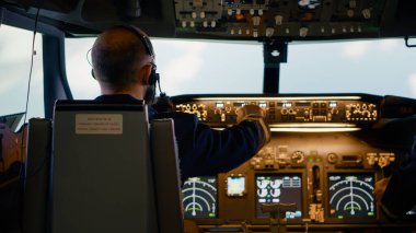 Erkek havayolu kaptanı yükseklik ve boylam düğmelerini tamir ediyor, kontrol paneli ve kontrol panelini kullanıyor. Hava mürettebatı ve radar pusulası, güç motoru ve ön camı olan bir uçak..