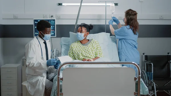 病人在医院病房接受医生的医疗援助 并戴口罩进行保护 大流行期间 医生一边与妇女交谈 一边帮助治疗静脉滴注袋 — 图库照片