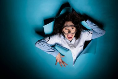 Manyak görünüşlü, laboratuvar patlamasından sonra kirli suratlı, deli bir bilim adamı mavi arka planda deli gibi davranıyor. Aptal kimyager, dağınık saç stili, kameraya bağırırken komik görünüyor..