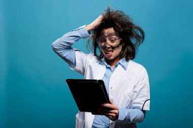 Kızgın biyokimyacı, deli gibi saç çekerken tabletle ilgili başarısız deney raporunu araştırıyor. Dokunmatik ekranlı öfkeli bir bilim adamı, mavi arka planda kirli bir yüz..