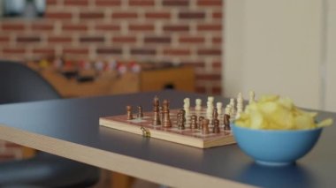 Empty living room table with chess board game and bowl of chips, no people in apartment used to meet and have fun with strategic activity. Nobody in space with checkmate play. Close up.