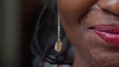 Makro bir fotoğraf, yüzünün yarısını kameraya gösteriyor, dudaklarında kırmızı ruj var. Makyaj malzemesi giyen, gülümseyen, mutlu ve otantik bir ifade sergileyen bir kadın model. Kapat..