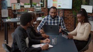 Afro-amerikan firması, analizleri dizüstü bilgisayar ve tablet istatistikleriyle planlamak için beyin fırtınası yapıyor. Mali tablolar ve grafikler oluşturmak ve takım çalışması yapmak için toplanan ofis çalışanları.