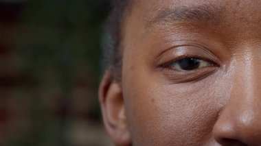 Genç bir yetişkinin gülümseyen ve kameraya bakıp bir gözünü ve yüzünün yarısını gösteren makro görüntüsü. Gözlerine odaklanan, kirpikleri, kaşları, göz bebeği, retinası ve gözü olan bir kadın modeli. Kapat..