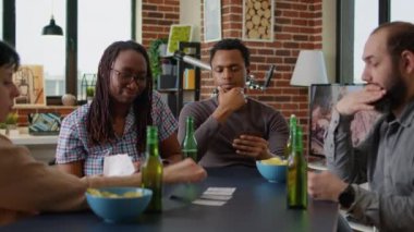 Portrait of african american man thinking about strategy play at card games with friends, having fun in living room. Young adult enjoying board game play with tactics, drinking beer with people.