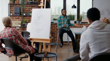 Yaratıcı insanlara tuvale resim çizmeyi öğreten genç bir adam resim tekniklerini resim dersinde pratik yapmak için kullanıyor. Öğretmen öğrencilere sanatsal vizyon ve ilham hakkında konuşuyor.