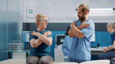 Ortopedi uzmanı fizyoterapi kontrolünde kıdemli hastaya kemik kırma pratiği yapıyor. Erkek terapist mekanik bozuklukları olan bir kadına kabinede hareket kabiliyetini artırması için yardım ediyor.