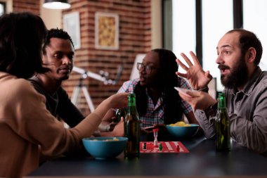 Birlikte tahta oyunları oynarken evde oturan neşeli, çok ırklı arkadaş grubu. Çeşitli insanlar masada oturup masa oyunları ve eğlence aktivitelerinin keyfini çıkarıyorlar..