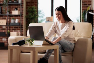 Başarılı otantik Asyalı kadın serbest yazar ev ofisinde çalışırken dizüstü bilgisayarda video yaratıcı fikirler izliyor. Çevrimiçi mutlu web 3.0 kullanıcı teknolojisi uygulaması