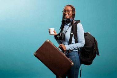 Fotoğraf cihazı ve kablosuz kulaklıkla seyahate çıkmayı bekleyen gülümseyen bir turist. Tatil çantalı ve DSLR kameralı mutlu gezgin tatile hazırlanırken kameraya iyimser gülümsüyor..