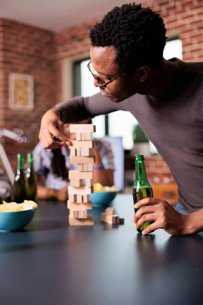 Hombre Afroamericano Enfocado Retira Cuidadosamente Bloque Madera Estructura Torre Madera — Foto de Stock