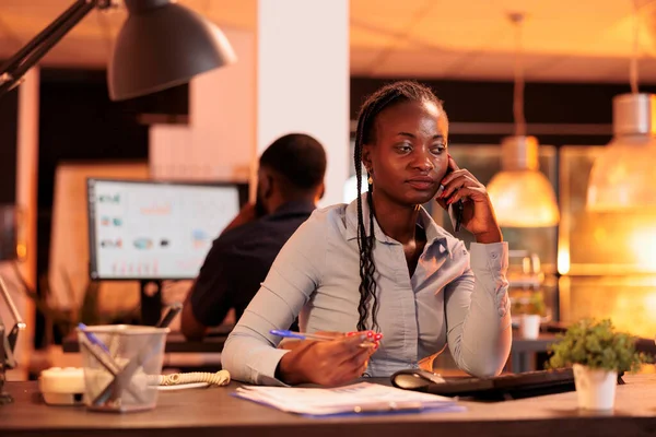 Young company worker chatting on smartphone call in office during sunset, having remote conversation about business report. Talking on mobile phone line about research data project.