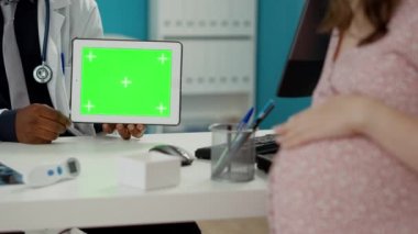 Hekim ve müstakbel anne dijital tabletteki yeşil ekrana bakıyor. Erkek sıhhiyeci boş kroma anahtar şablonu tutuyor. İzole edilmiş telif alanı ve model arka planı var. Kapat..