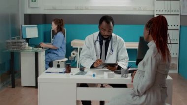 Pratisyen hekim hamile bir hastaya doğum kontrolünde dijital tabletle ilgili notlar alıyor. Erkek doktor, müstakbel annesiyle muayenehanede hamilelik hakkında konuşuyor..