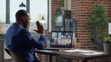 Young businessman attending teleconference meeting on laptop, talking to colleagues on online videocall conference. Chatting on videoconference for remote telecommunication with headphones.