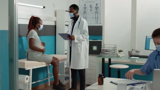アフリカ系アメリカ人の医療と妊娠中の患者は コロナウイルスパンデミックの際に任命で会う 妊娠中のお腹の女性と話す医師 健康診断のアドバイスを受ける — ストック動画