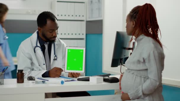 医務室のデジタルタブレットで緑の画面を見て 赤ちゃんのバンプを持つ医師と女性 医師と患者は 空白のモックアップコピースペースと隔離されたクロマキーテンプレートを分析します — ストック動画