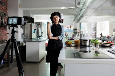 Şef, profesyonel bir restoranda yemek kursunu çekerken kameranın önünde yürekten gülümsüyor. Çevrimiçi platform ve televizyon programı için mutfak videosu çeken kendine güvenen aşçı.