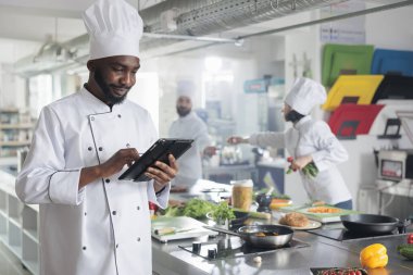 Lokanta mutfağında yemek tarifleri ararken el bilgisayarı konusunda gastronomi uzmanı. Tablet beyin fırtınası yapan baş aşçı gurme yemek için garnitür fikirleri üretiyor..