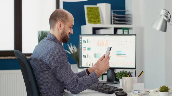 Male worker looking at text message on mobile phone app, taking break after working on financial statistics. Executive assistant using smartphone to browse internet and plan strategy.