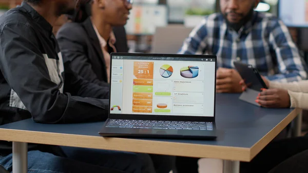 African american team of colleagues meeting in boardroom to work on financial charts, analyzing statistics and diagram reports on laptop. Computer screen with investment value. Close up.