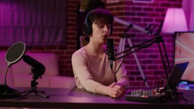 Masadaki stüdyodan profesyonel mikrofon kullanarak konuşma programı yayınlarken gülümseyen kulaklıklı kadın portresi. Canlı çevreleme programı için internet radyo sunucusu yayınlama içeriği .