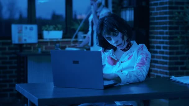 同僚が夜に固定電話で話している間 現代のノートパソコンで働いているゾンビの女性を見てゾンビ ポータブルコンピュータを使用して会社のワークスペース内で奇妙な恐ろしい脳食べるモンスターと — ストック動画