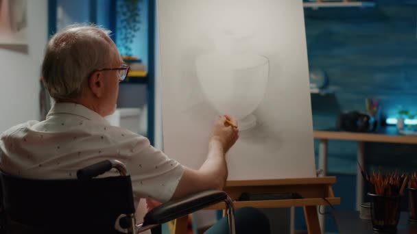 男性の車椅子ユーザーは プロのツールや機器を使用して キャンバス上の花瓶のデザインスケッチを描く 身体障害や健康状態に悩まされながら 作品の傑作を描く — ストック動画