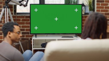 Erkekler ve kadınlar evlerinde modern teknolojiyi kullanarak yeşil ekranlı televizyon izliyorlar. İnsanlar izole edilmiş şablon ve kopya alanı ile boş krom anahtar arka planına bakıyorlar. Kapat..