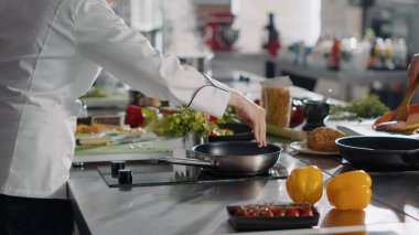 Genç bir kadın mutfak ocağında sarımsaklı karanfille yemek tarifi pişiriyor ve restoran yemeği hazırlamak için tavaya aromatik malzemeler ekliyor. Üniformalı şef yemek hazırlıyor. El kamerasıyla..