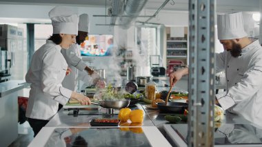 Çeşitli aşçı takımları gurme yemekleri hazırlıyor, fırında lezzetli yemekler pişiriyor. Beyaz üniformalı insanlar sebzelerle organik gastronomi yemeği yapmak için profesyonel tarif kullanıyorlar..