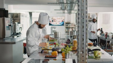 Restoran mutfağında İtalyan yemeği tarifi için rendelenmiş peynir yapan profesyonel bir aşçı. Üniformalı bir erkek aşçı lezzetli yemek hazırlamak için parmesan peyniri rendeliyor..