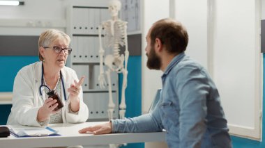 Kadın doktor, reçeteli ilaçları şişede açıklıyor, genç hastaya sağlık kontrolünde hap, ilaç ve ilaç veriyor. Vitamin ve ağrı kesicilerle ilaç tedavisi.