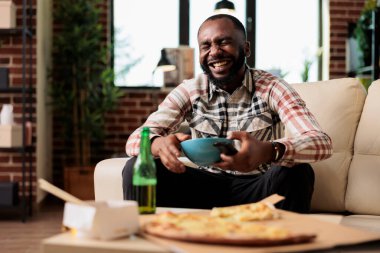 Televizyondaki komedi filmine gülen, kaseden cips yiyen, paket servis yemeği ve bira getiren neşeli bir adam. Televizyonda filmle eğlenmek ve hazır yemek yemek yemek..