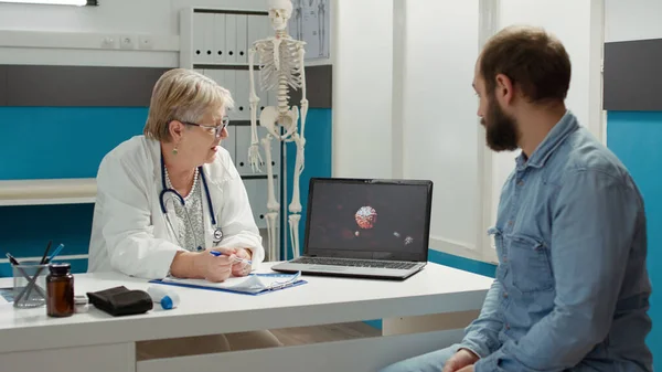 Health specialist showing coronavirus illustration on laptop, explaining disease diagnosis to young patient at checkup appointment. Analyzing virus animation for recovery in cabinet.