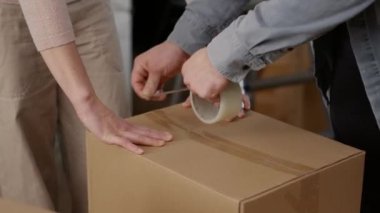 Çift karton kutulara bir şeyler koymak için yapışkan bant kullanıyor, karton kutuları yapışkan silindirle paketliyor. Nakliye için paketler hazırlanıyor. Taşınmak için. Kapat..