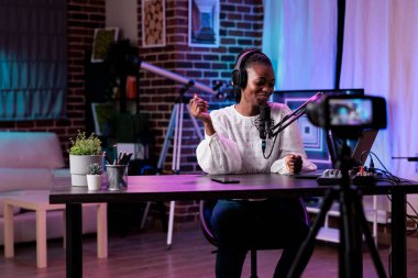 Afrikalı Amerikalı blog yazarı çevrimiçi podcast programı çekiyor, kamera karşısında kanal izleyicileriyle konuşuyor. Sosyal medya içeriği ve rpg ışıkları stüdyosu yaratmak için internet üzerinden canlı video kaydeden kadın etkileyicisi.