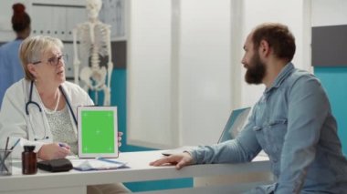 Doktor, kabinedeki dijital tablette yeşil ekranı dikey olarak tutuyor. Check-up 'taki insanlar görüntüde izole edilmiş kromakey arkaplan ve boş telif alanına sahip şablona bakıyorlar.